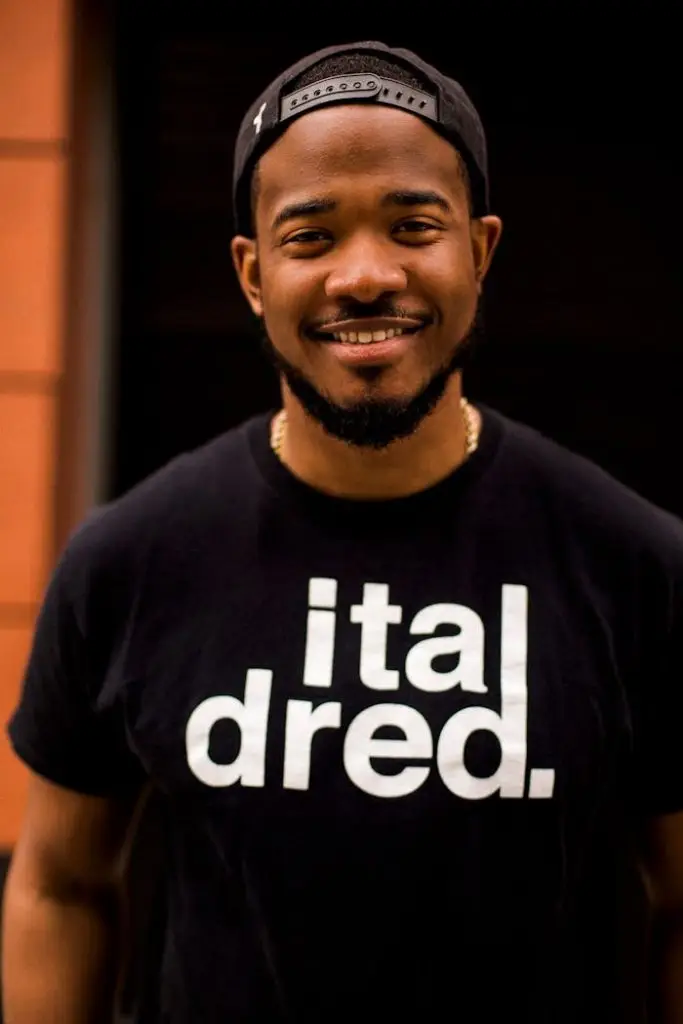 Portrait of a smiling man wearing a black t-shirt and cap outdoors.