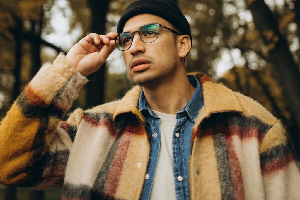 Mastering the First Impression: Your intriguing post title goes here A fashionable man with eyewear and a checkered coat thoughtfully posing in a serene fall setting.